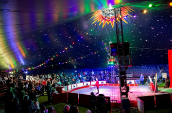 Photograph of a circus in a big top with bright coloured lights and performers