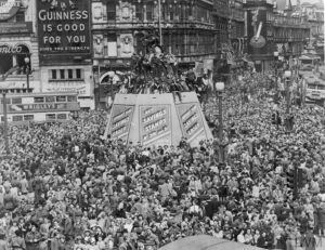 A black and white photograph of Piccadilly in London on VE Day in 1945 with crowds filling the space. 